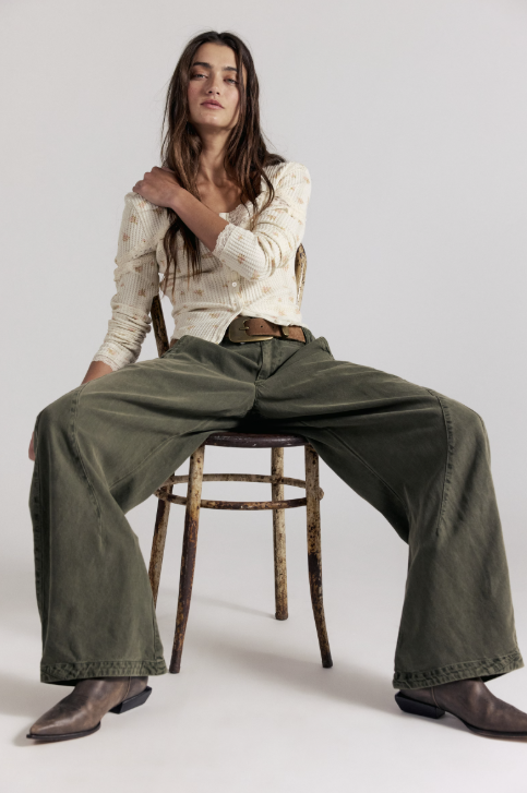 Woman sitting in chair wearing green pants and white top on grey background