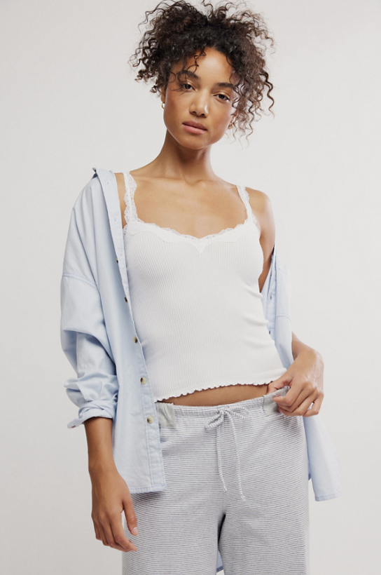 Woman wearing a light blue hoodie over a white tank top and striped pants on a plain background