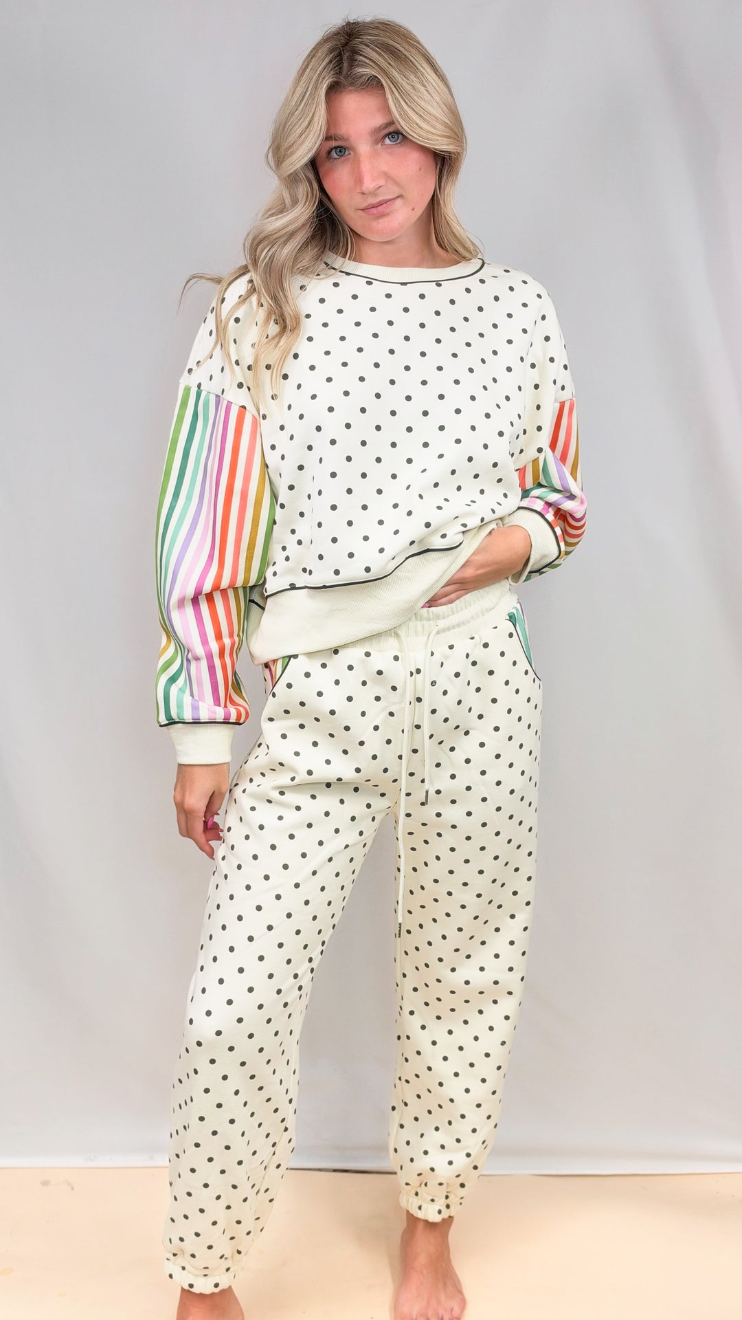 Woman wearing matching cream set with rainbow color stripe sleeves and polka dots on plain background