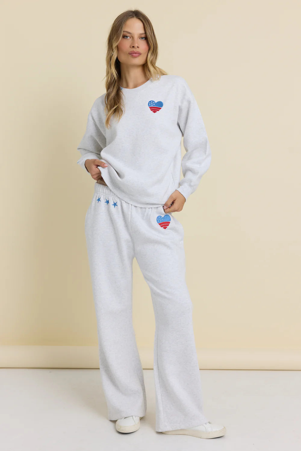 Woman wearing a light gray sweatshirt and white pants with heart designs on a beige background