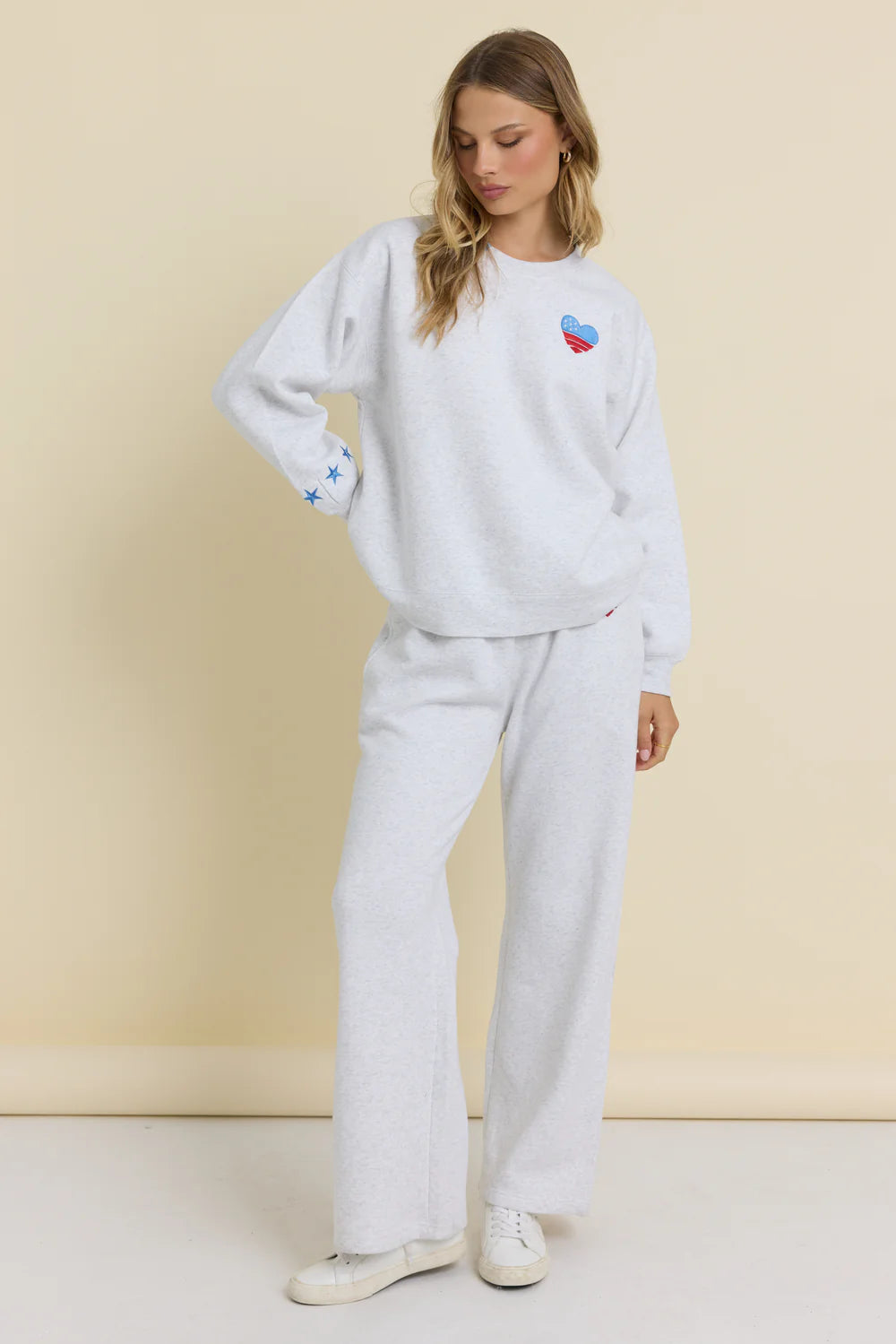 Woman wearing a white sweatshirt and pants with colorful designs against a beige background