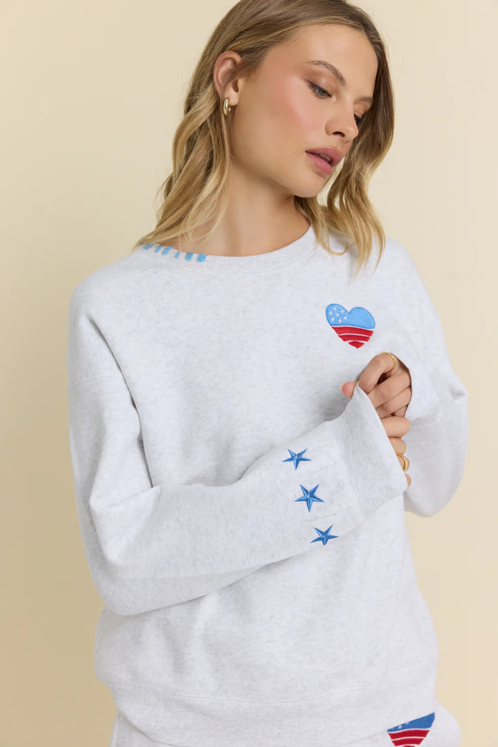 Woman wearing a light gray sweatshirt with star and heart designs on a beige background