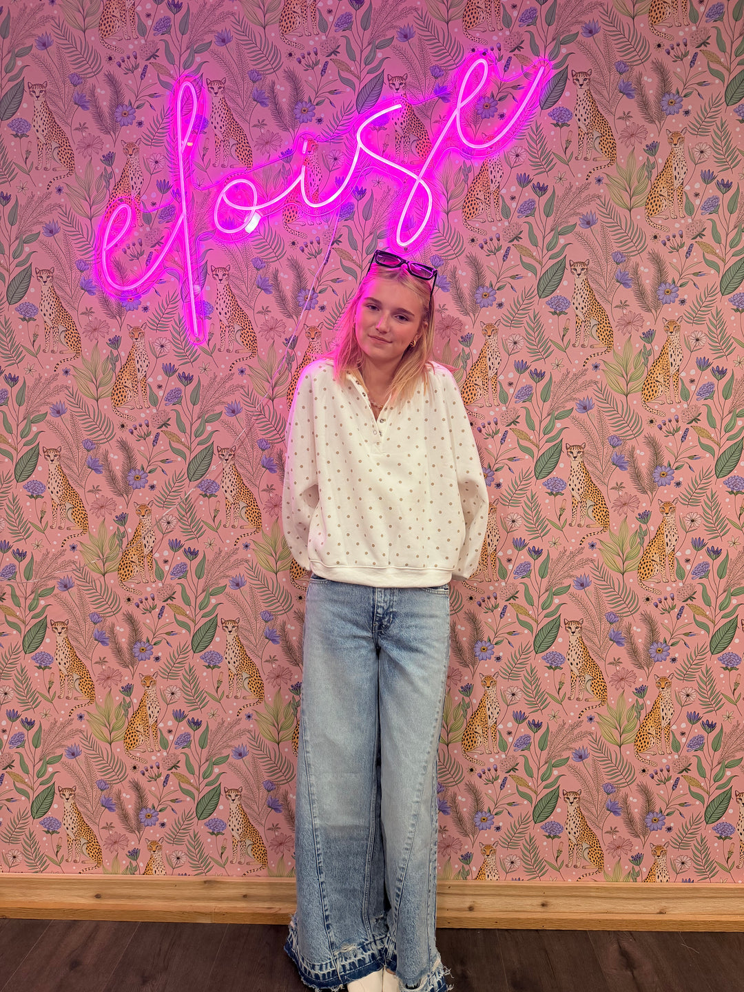 Person lying on a pink floral-patterned floor with a neon sign spelling 'LOVE' nearby.