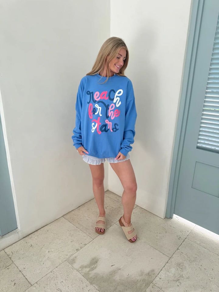 Woman wearing a blue sweatshirt with text, standing in a room with light-colored floor and white walls.