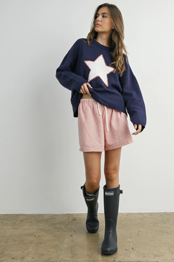 Woman wearing blue sweater with white star and stitching on plain background
