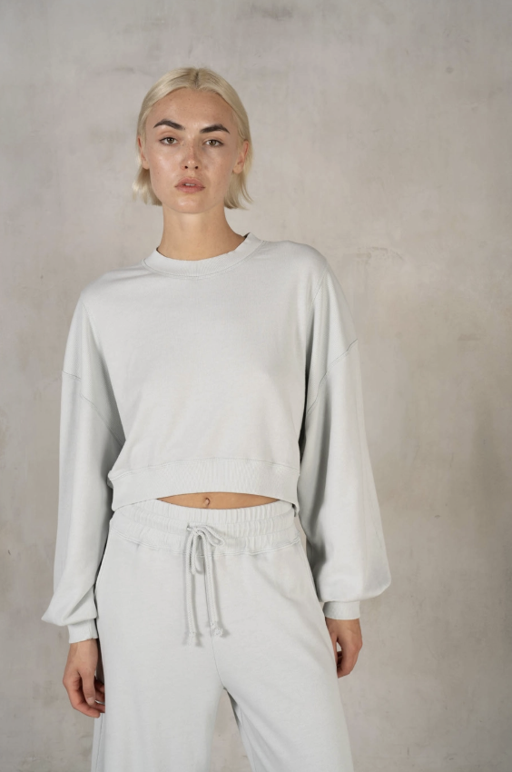 Person wearing a light gray sweater and pants against a plain background