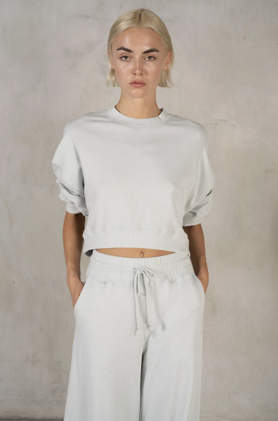 Person wearing a light gray sweater and white pants against a plain background