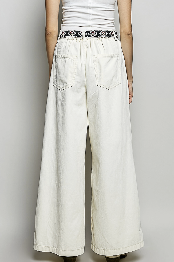 Person wearing white wide-leg pants with a patterned belt on a plain background