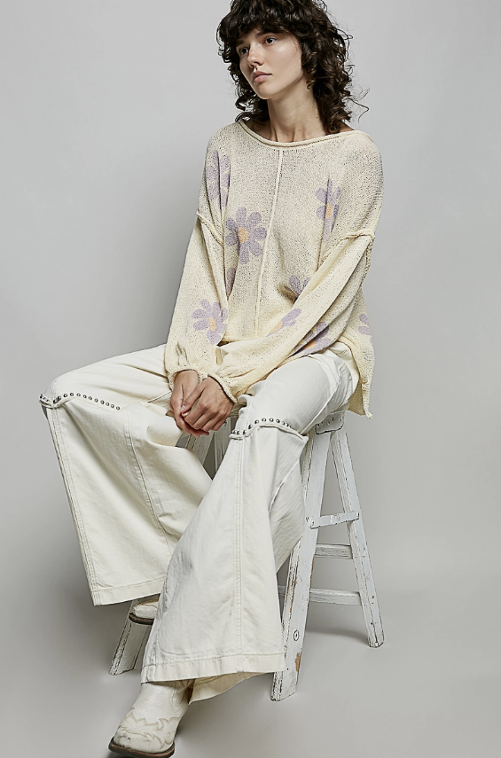 Person wearing a light-colored outfit with floral patterns, sitting on a stool against a plain background.