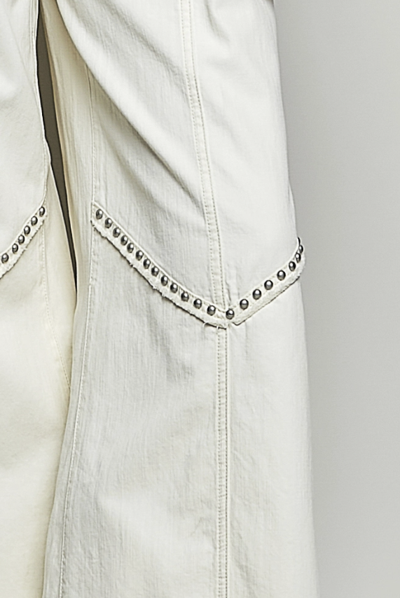 Close-up of a white denim jacket with studded details on a light gray background