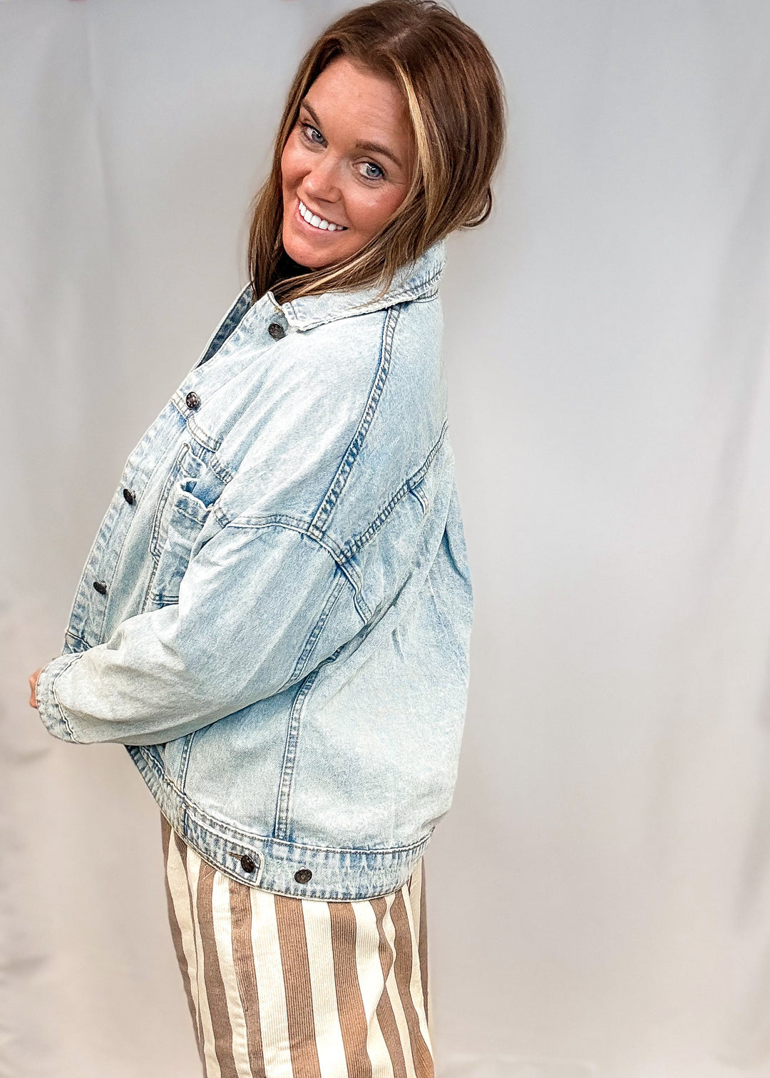 Woman wearing beige and white stripe pants and jean jacket on white background