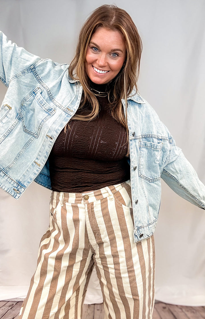 Woman wearing beige and white stripe pants with brown top and jean jacket on white background