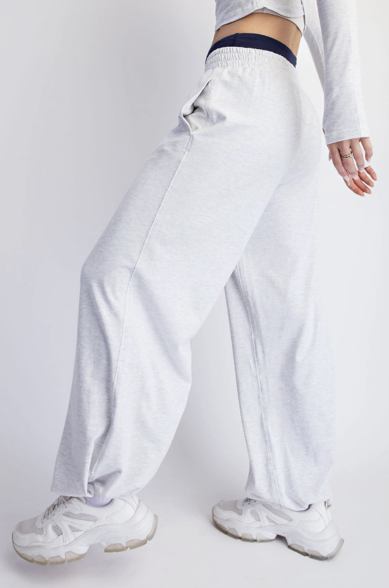 A person wearing light heather gray wide-leg sweatpants with a dark navy elastic waistband, styled with white sneakers against a plain light gray studio background.