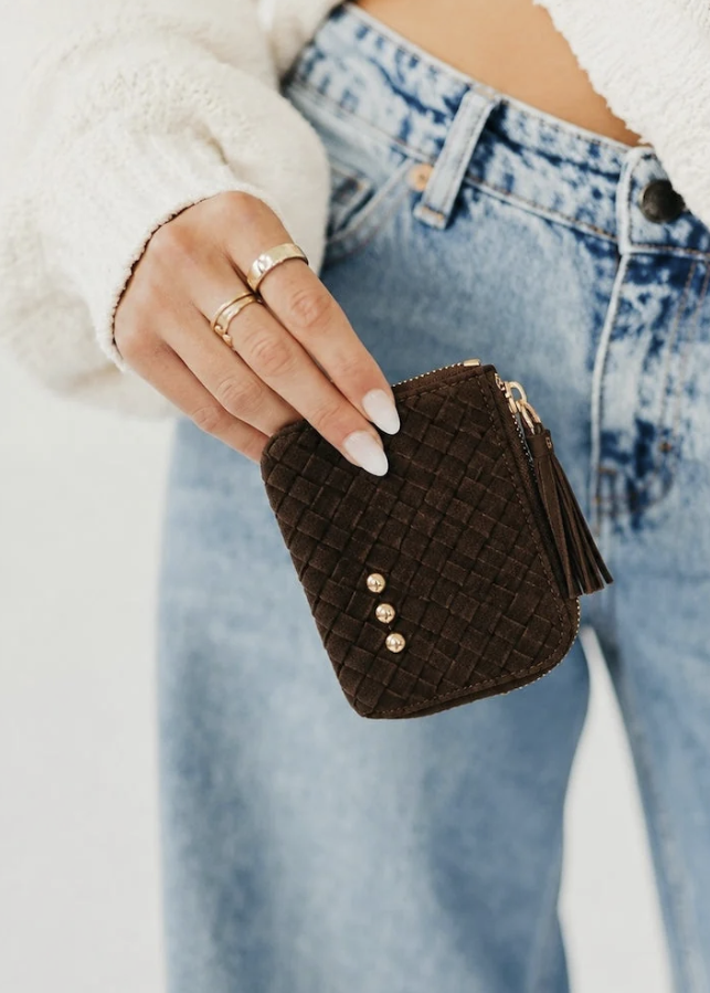 Woman wearing cream sweater and jeans holding a chocolate card wallet on white background