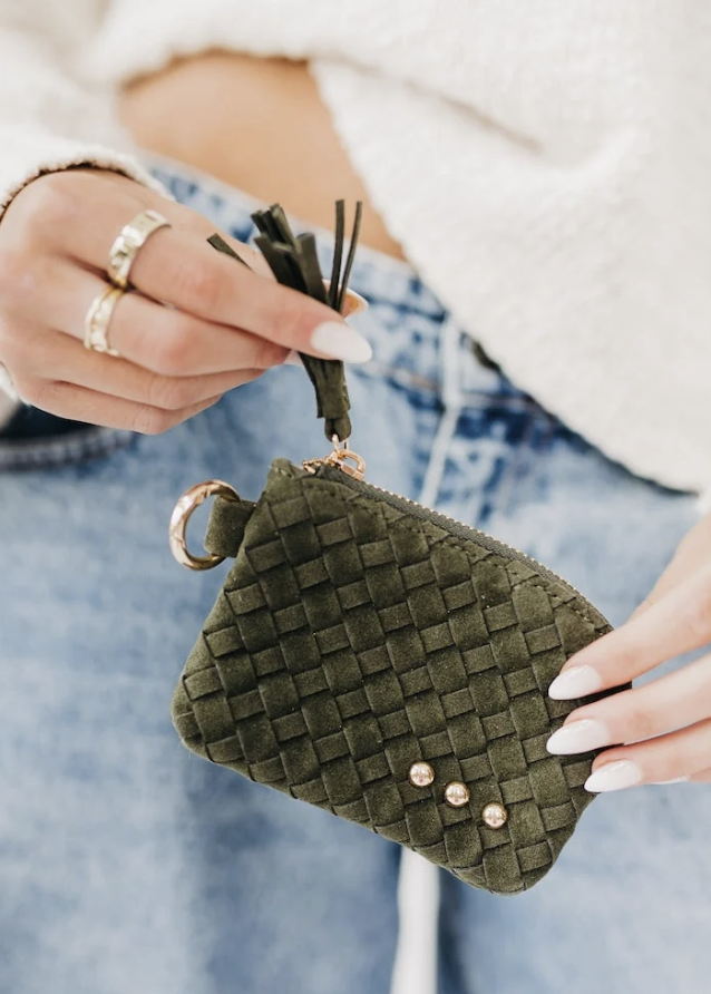 Woman wearing cream sweater and jeans holding an olive suede card wallet on white background