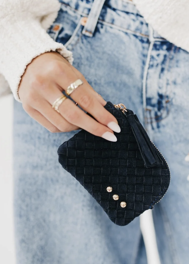 Woman wearing cream sweater and jeans holding navy suede card wallet on white background