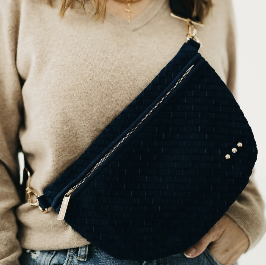 A navy blue woven crossbody bag with gold-tone hardware, worn diagonally across the chest of a person wearing a beige sweater and jeans.