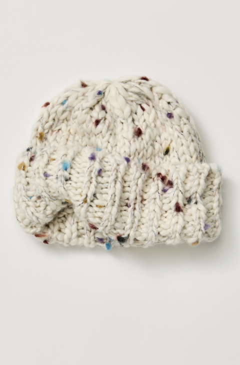 Chunky cable-knit beanie hat in off-white yarn with multicolored flecks, photographed flat on a light gray background.
