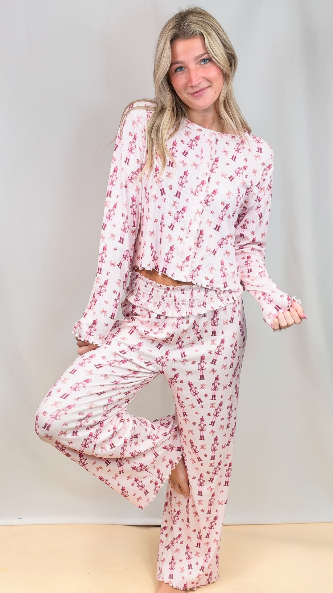 Woman wearing pink christmas pajamas with nutcrackers on plain background
