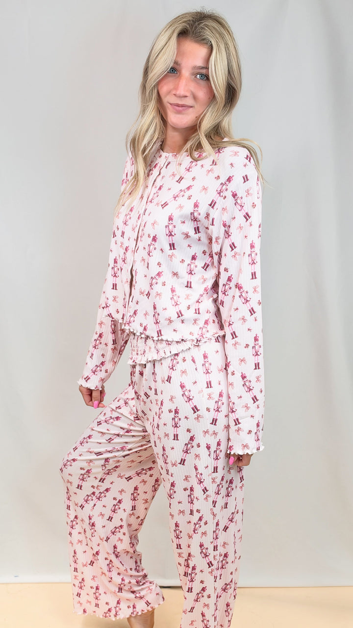 Woman wearing pink christmas pajamas with nutcrackers on plain background