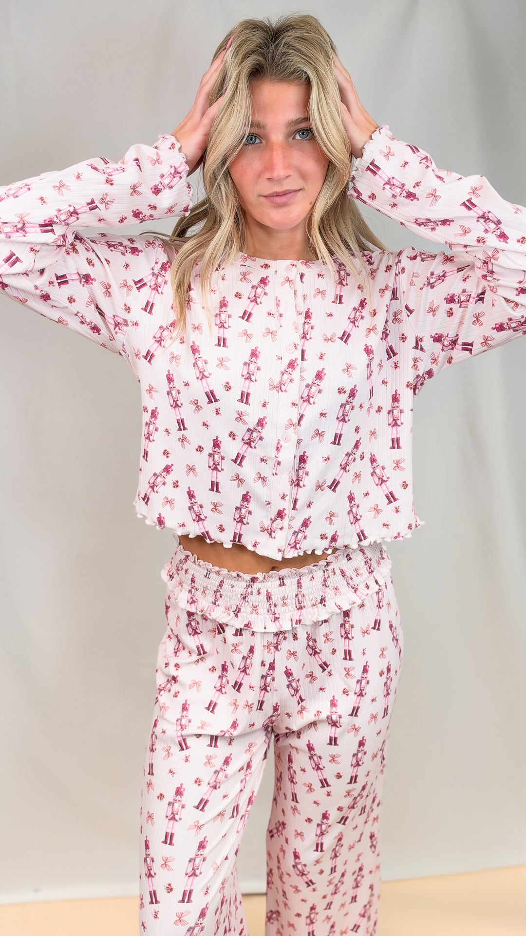 Woman wearing pink christmas pajamas with nutcrackers and bows on plain background
