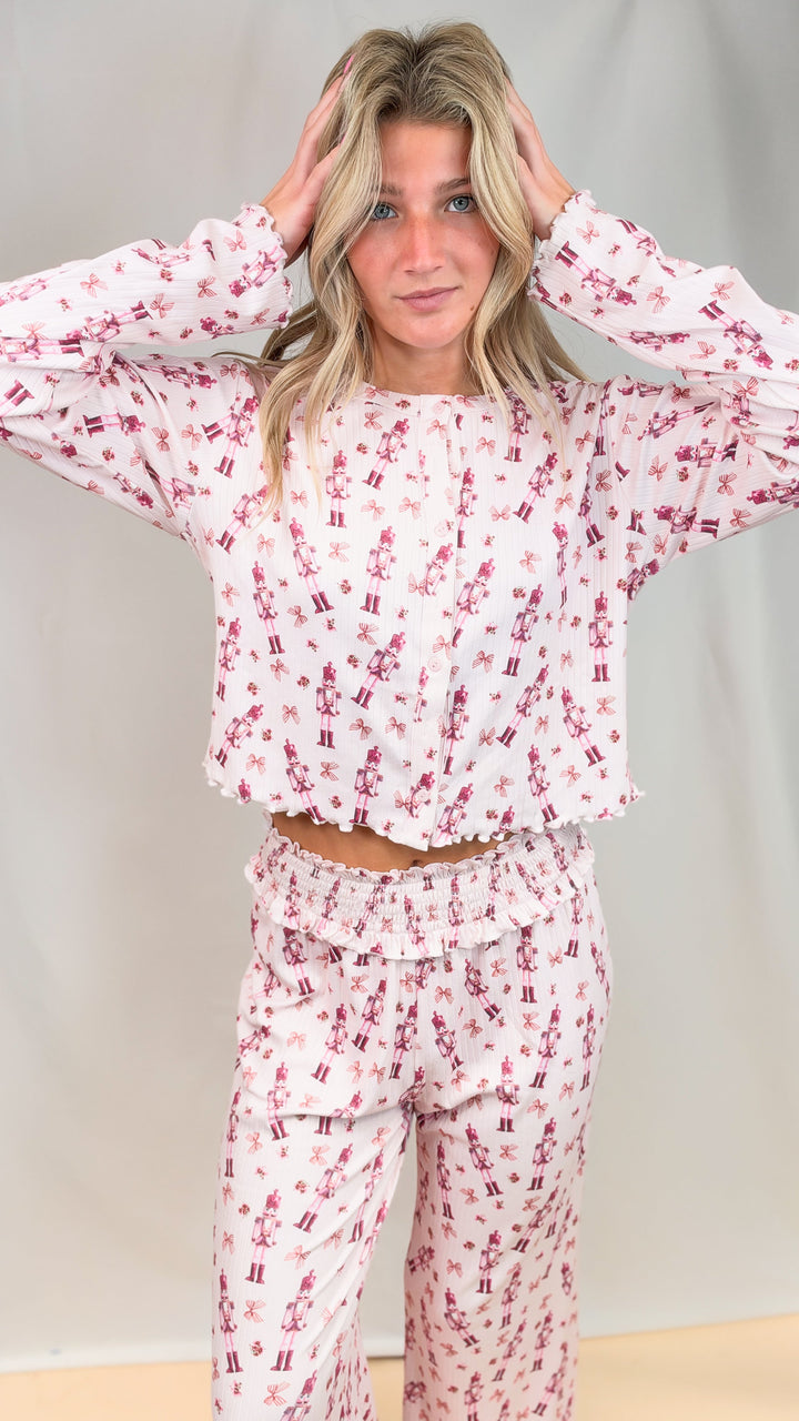 Woman wearing pink christmas pajamas with nutcrackers and bows on plain background