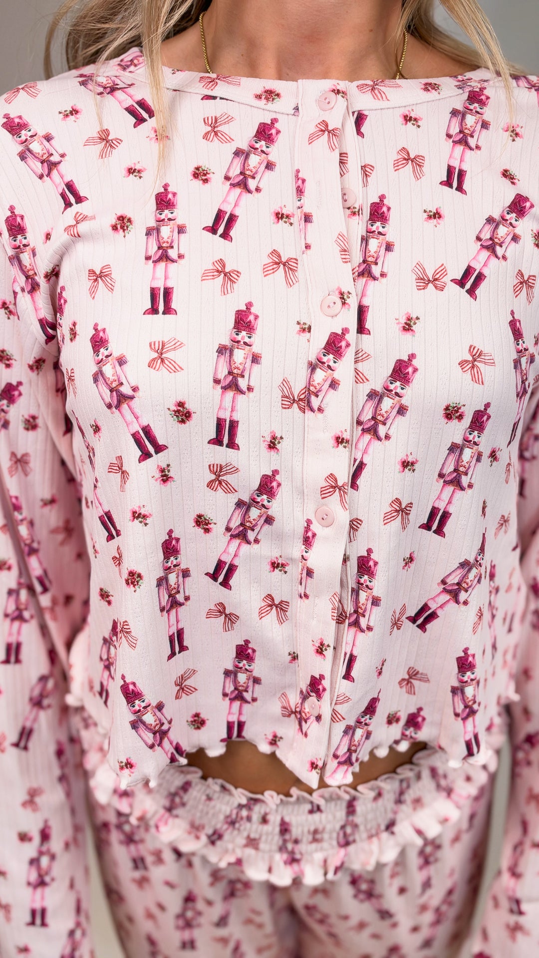 Close up of woman wearing pink christmas pajamas with nutcrackers and bows on plain background