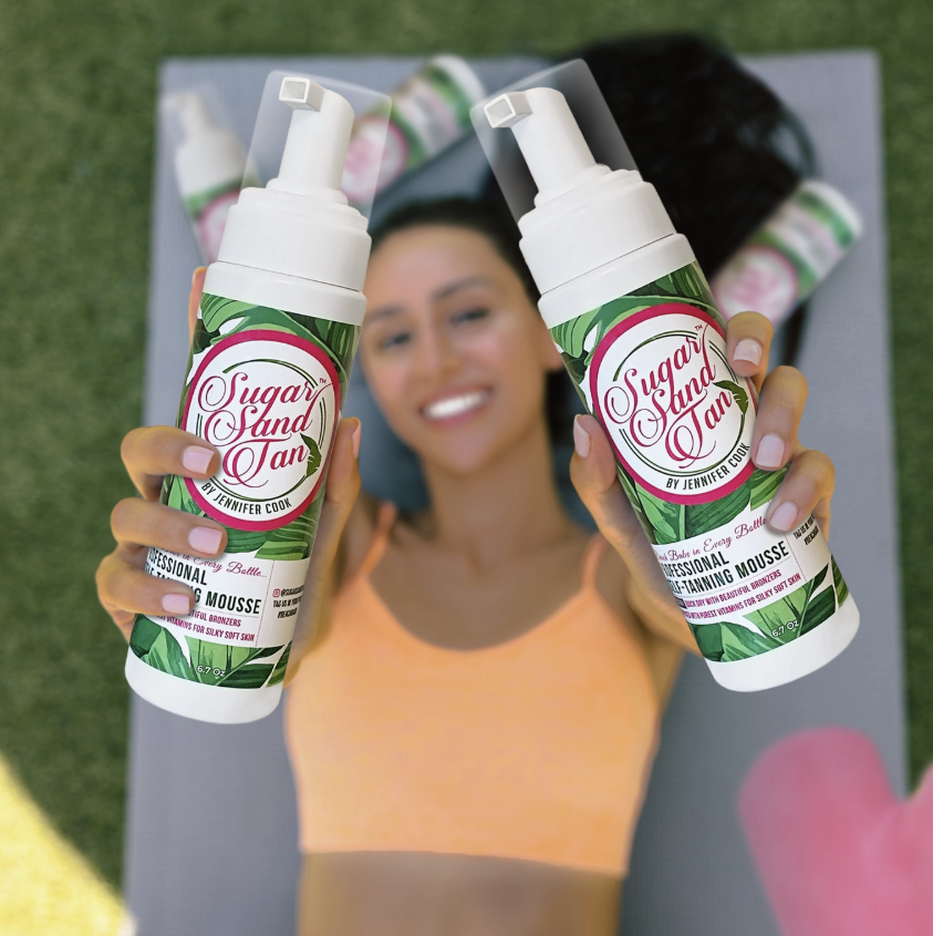 Woman holding self tanning products while laying on towel