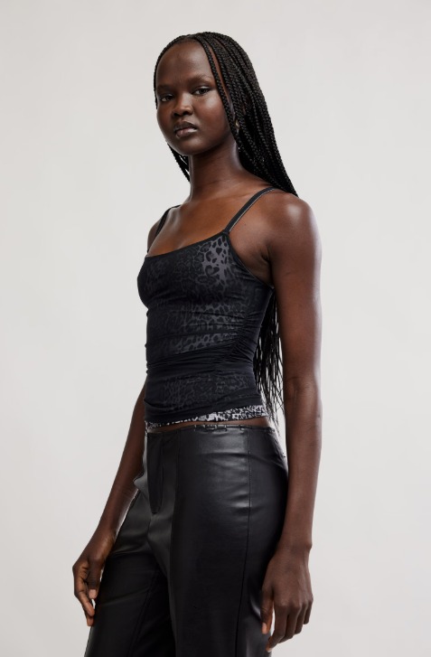 Woman wearing a black top and leather pants against a plain background