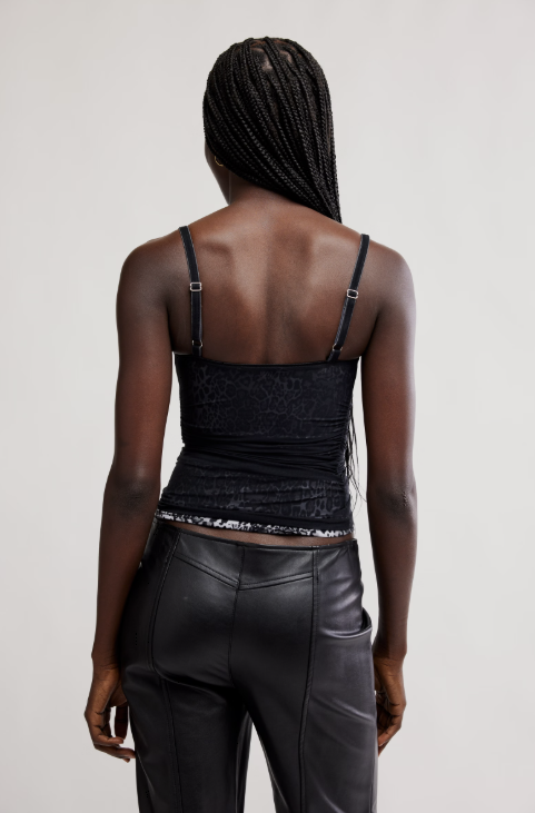 Person wearing a black strappy top and leather pants on a plain background