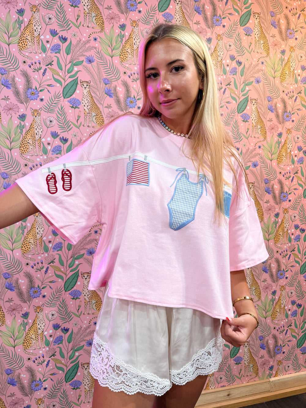 Person wearing a pink oversized shirt with graphic designs against a pink background with animal and floral patterns.