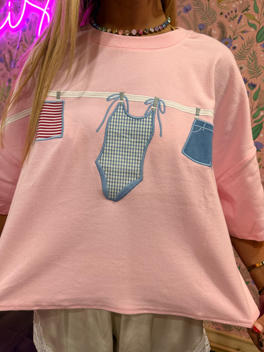 Pink sweatshirt with graphic of a swimsuit and jeans on a patterned background