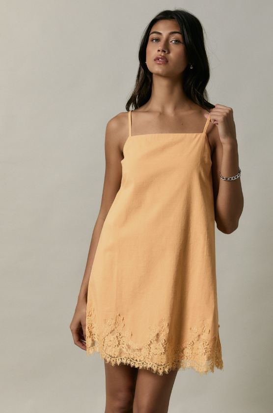 Woman wearing orange dress with lace trim on plain background