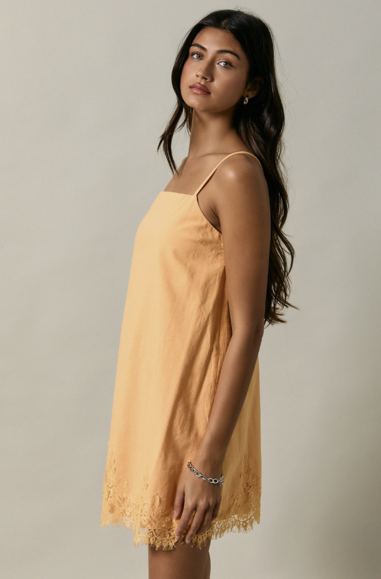 Woman wearing a light yellow dress with thin straps against a neutral background