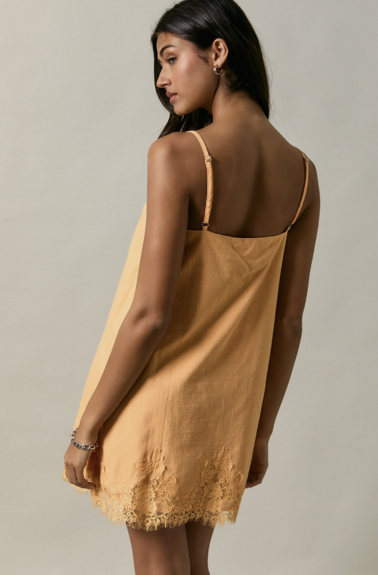 Woman wearing an apricot color slip dress with thin straps on a neutral background