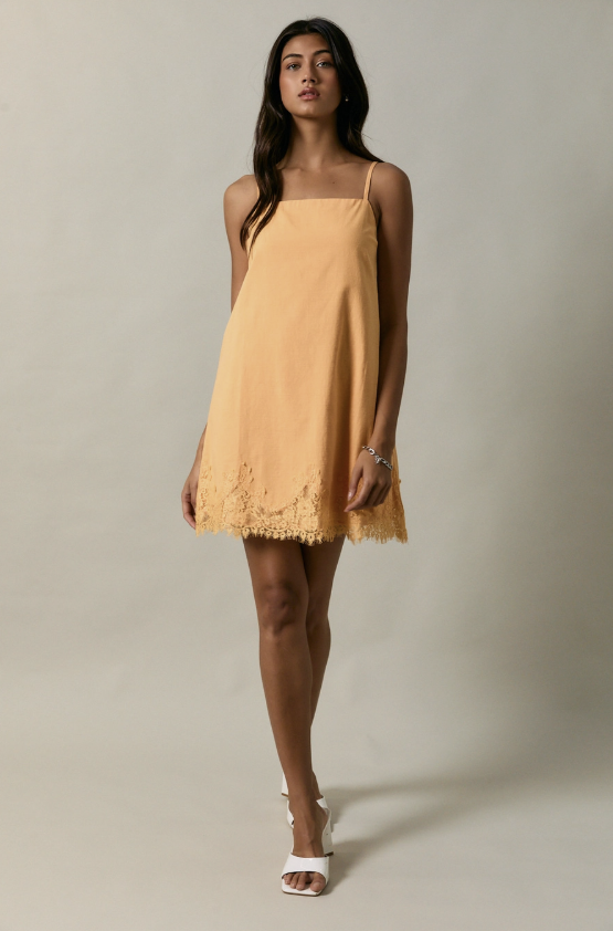 Woman wearing an apricot color dress with lace details on a plain background