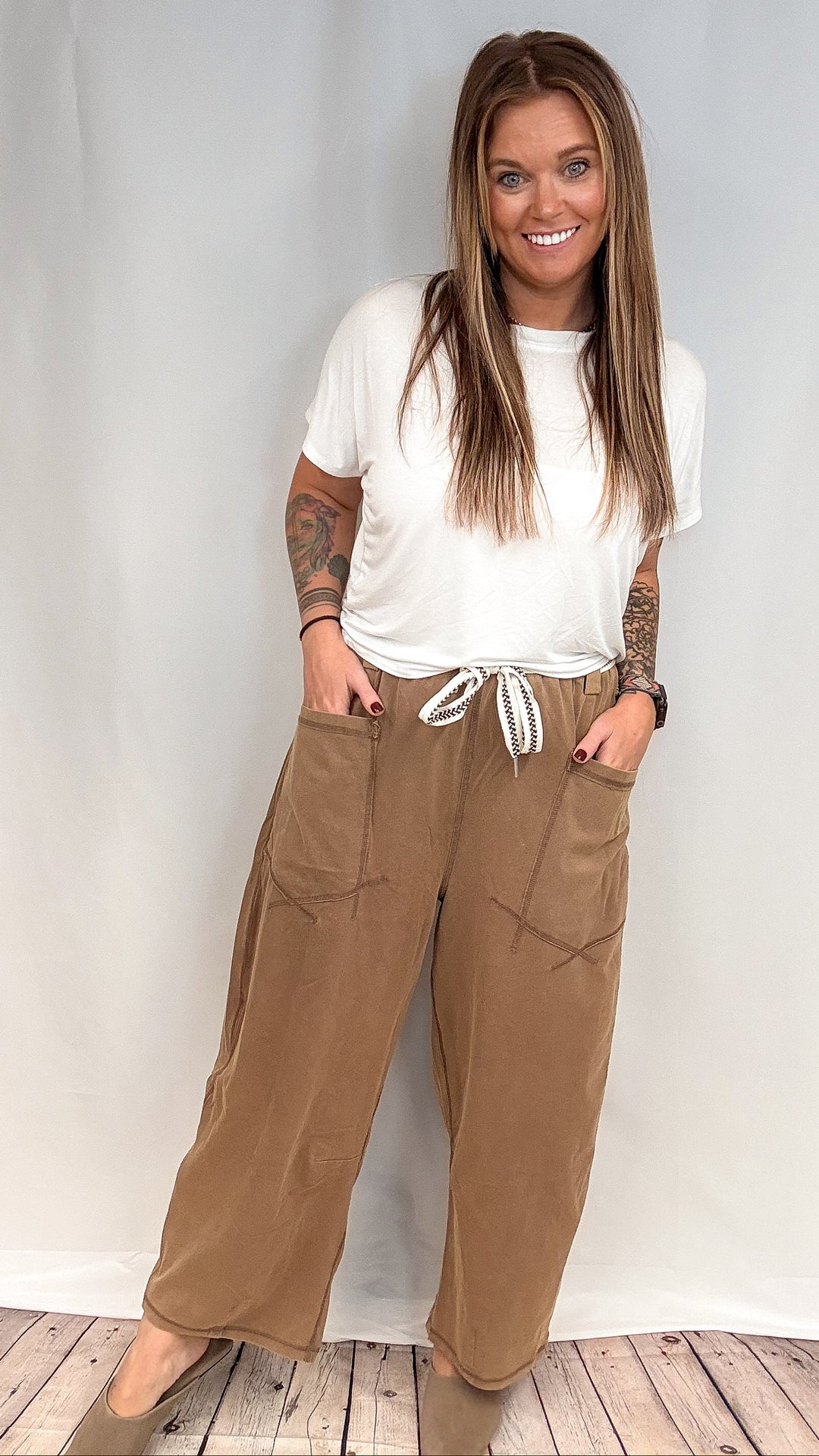 Woman wearing white short sleeve shirt and brown barrel sweatpants on white background