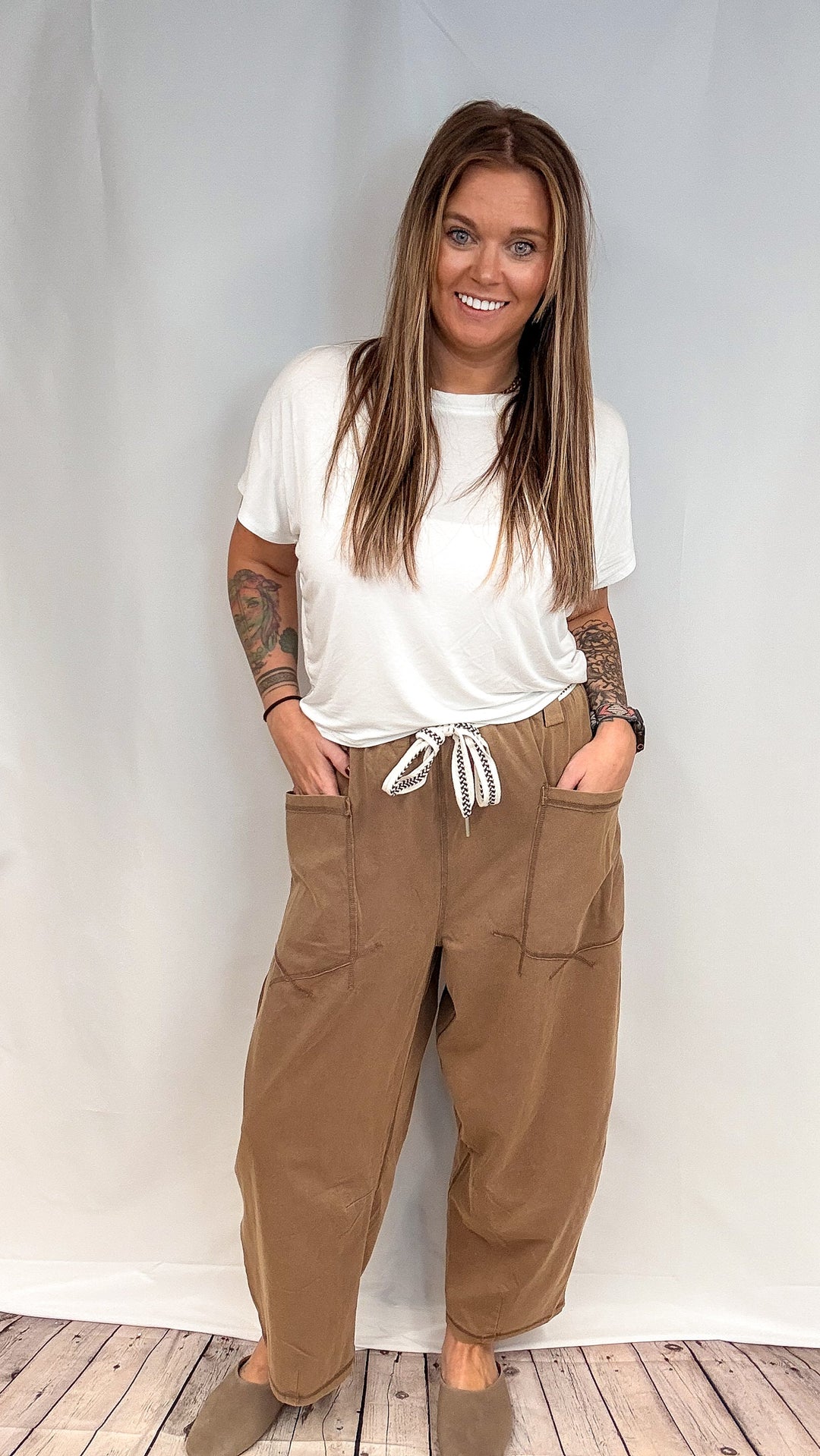 Woman wearing white short sleeve shirt and brown barrel sweatpants on white background