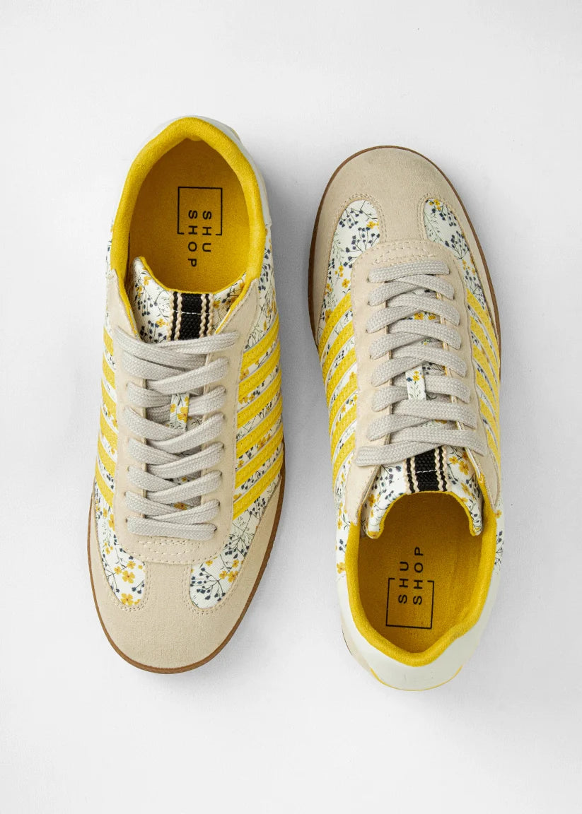 Sneakers with yellow and floral accents on plain background