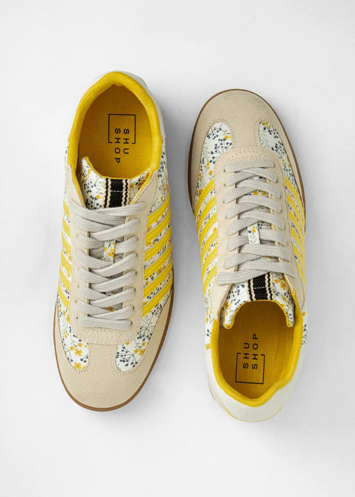 Sneakers with yellow and floral accents on plain background