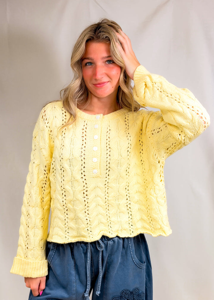 Woman wearing yellow cable knit henley pullover on plain background