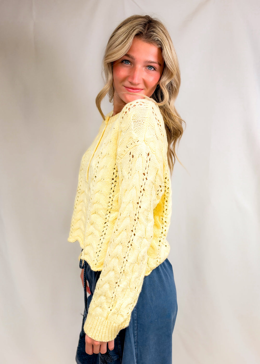 Woman wearing yellow cable knit henley pullover on plain background