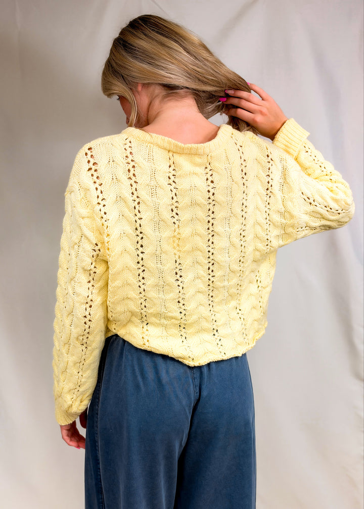Woman shown from back wearing yellow cable knit pullover on plain background