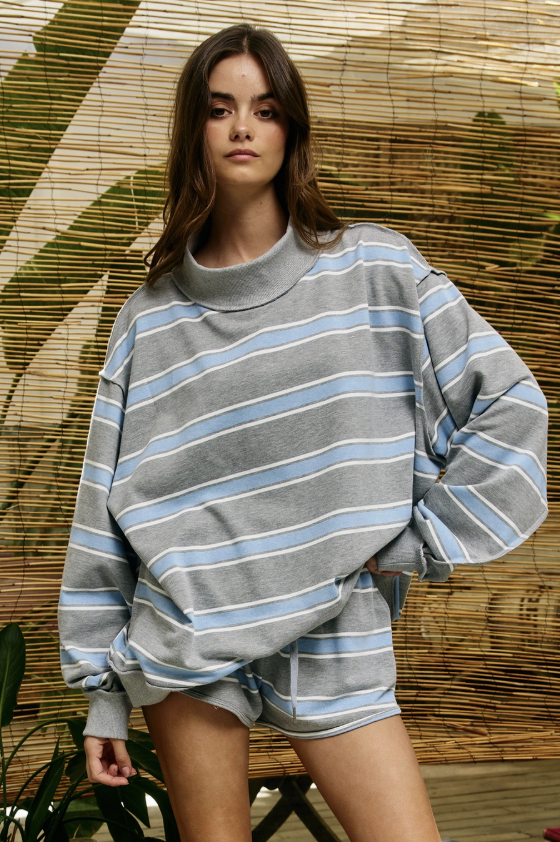 Woman wearing blue and grey striped mock neck sweatshirt and matching shorts in front of bamboo wall