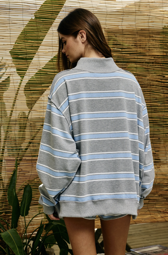 Back of woman wearing blue and grey striped mock neck sweatshirt in front of bamboo screen