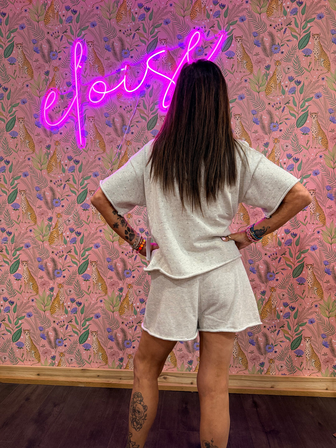Back of woman wearing matching grey top and shorts on pink floral background