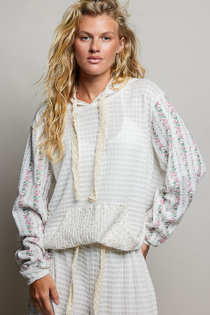Woman wearing a white floral blouse and pants against a gray background