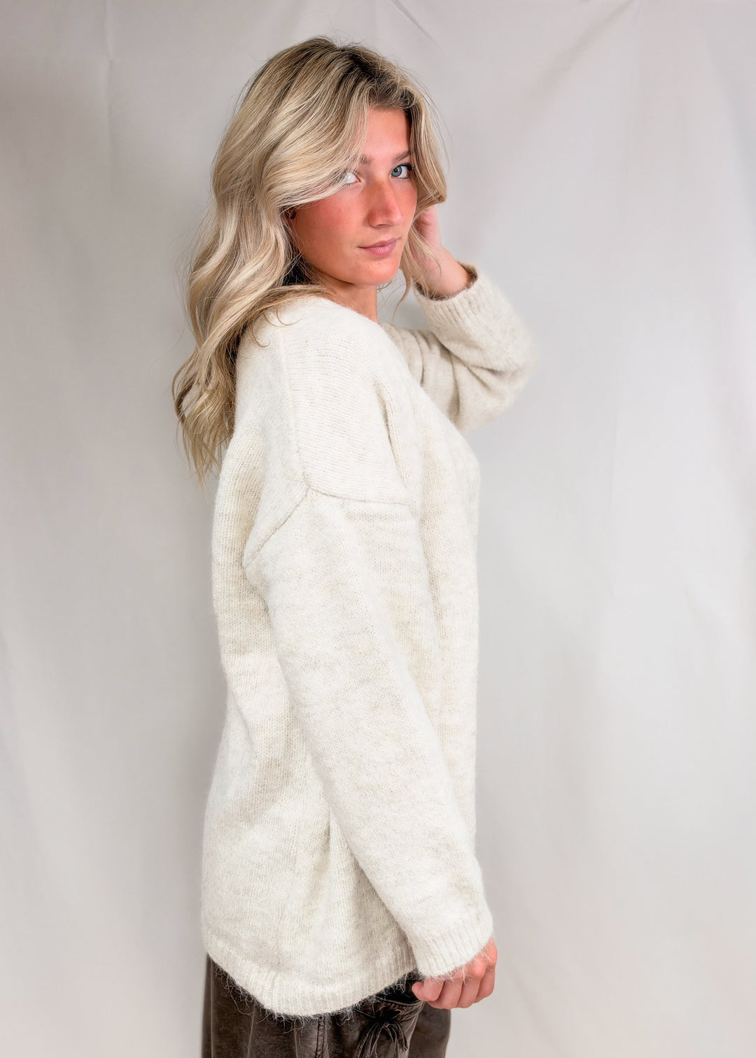 Woman wearing cream cardigan and brown pants on plain background