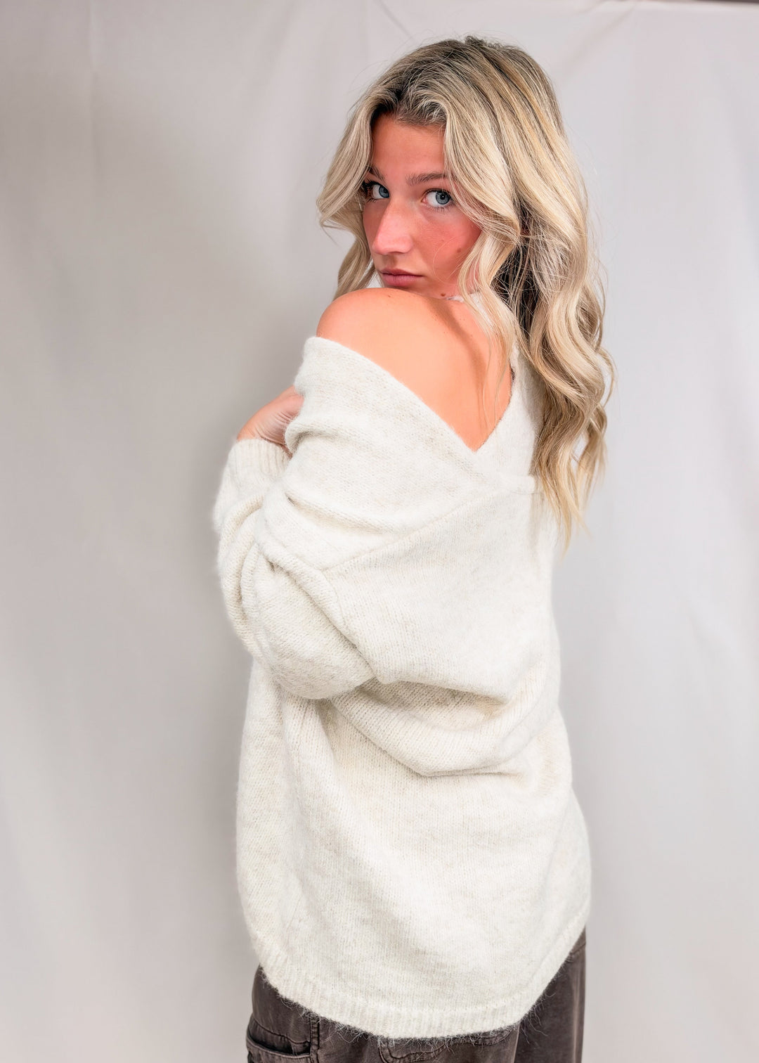Woman wearing matching cream cardigan and tank with brown pants on plain background