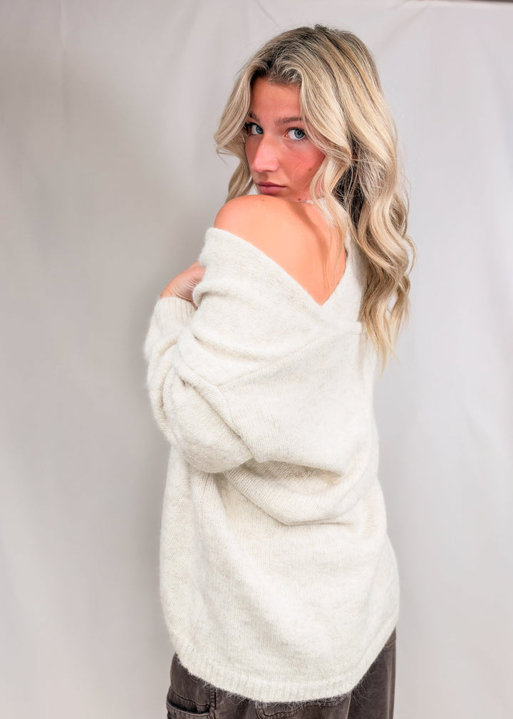 Woman wearing matching cream cardigan and tank with brown pants on plain background